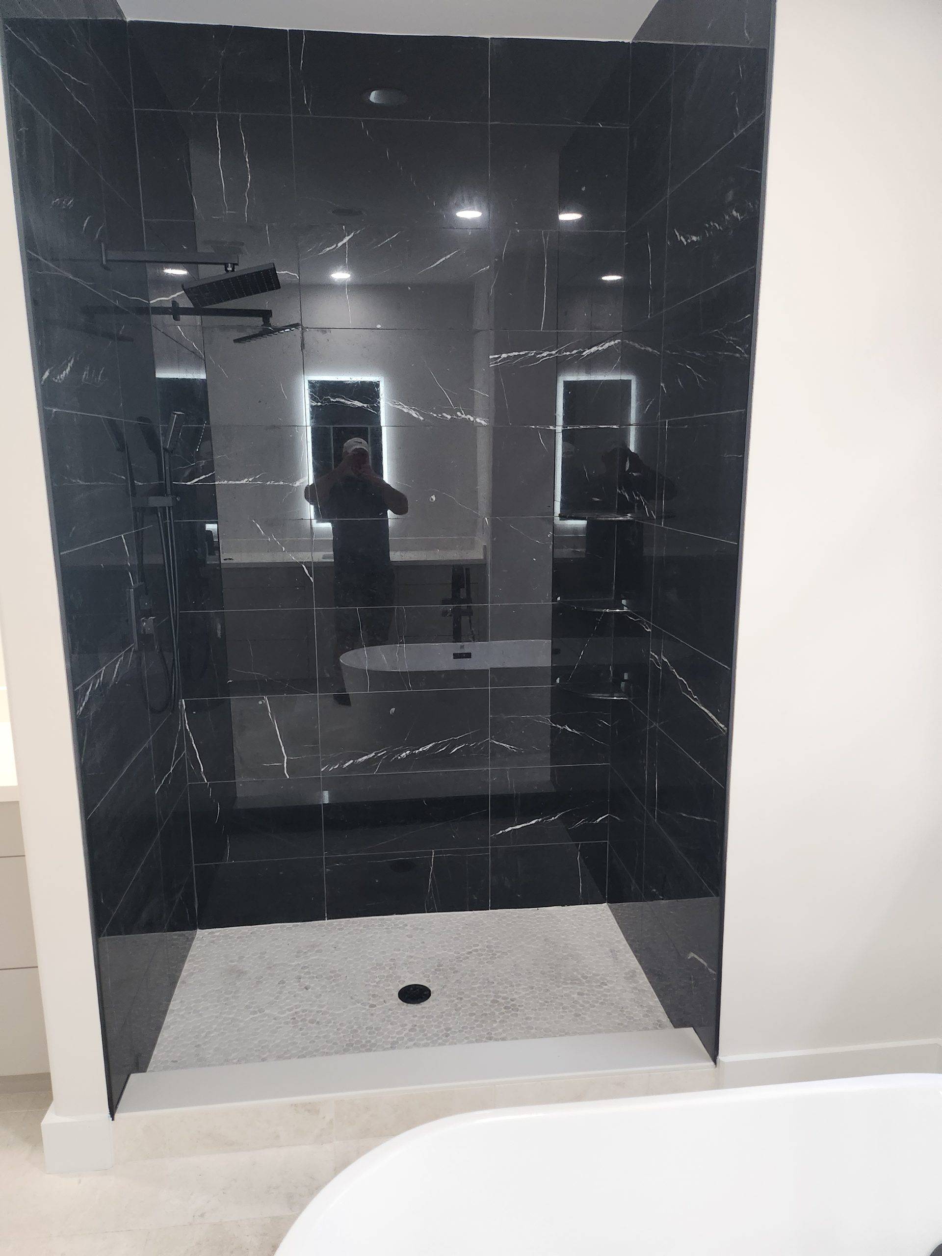 Walk-in shower with black marble-look tile walls and a white pebble mosaic floor