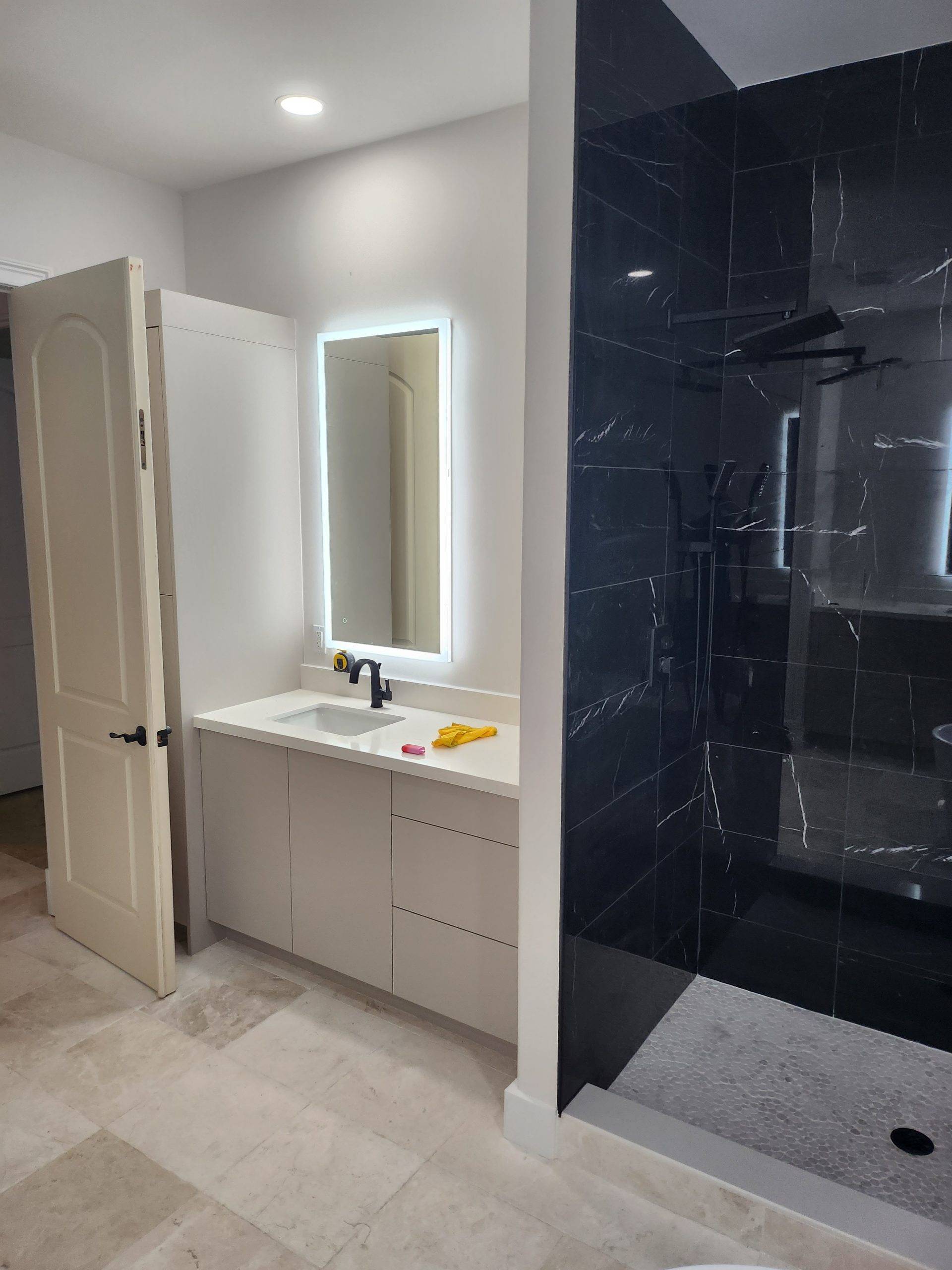 Bathroom vanity with a backlit mirror next to a black marble-look tile shower