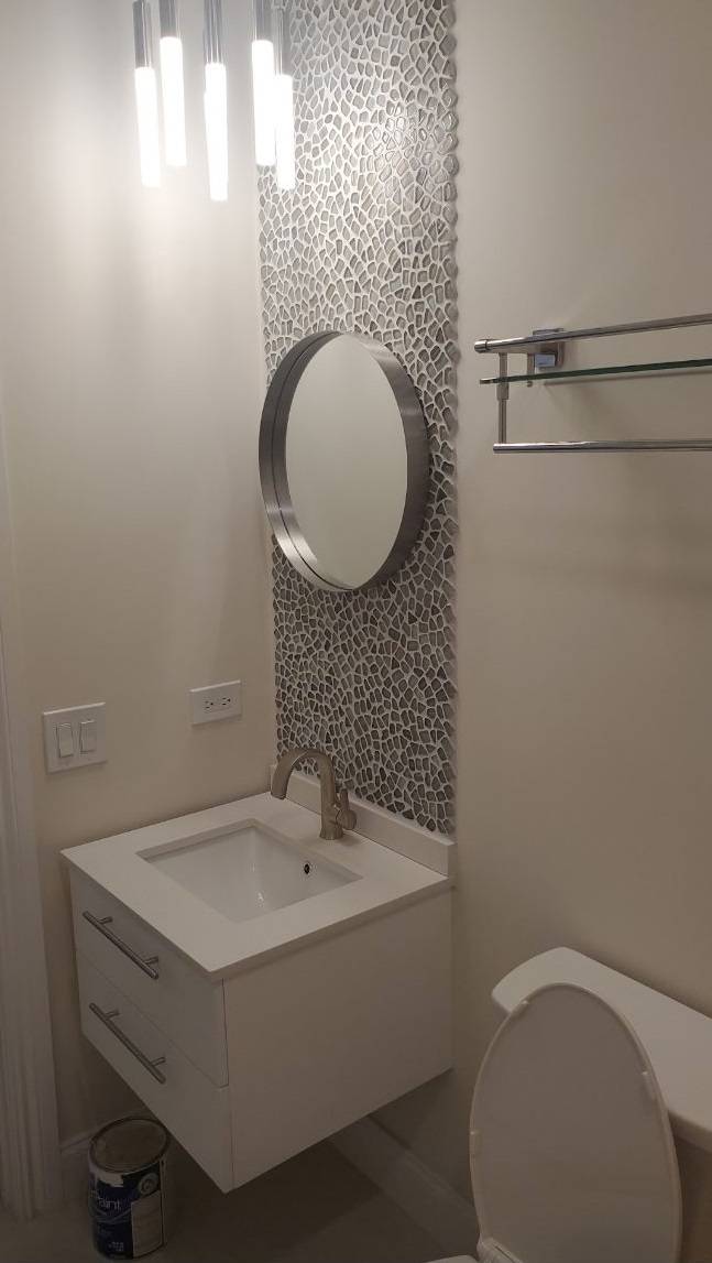 Bathroom remodel with a floating white vanity, round mirror, and pebble mosaic tile accent wall