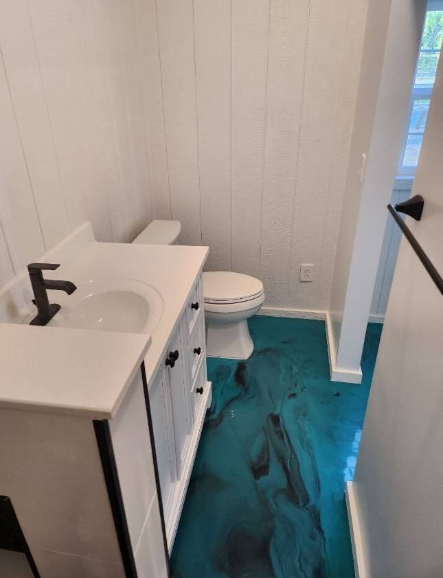 Bathroom with a white vanity, black fixtures, and a glossy teal epoxy floor