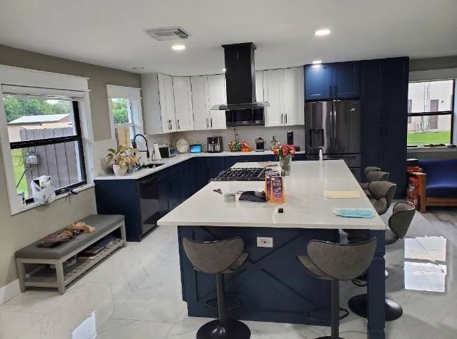 Remodeled kitchen with navy-blue cabinets, a white island with seating, and marble-look tile floors