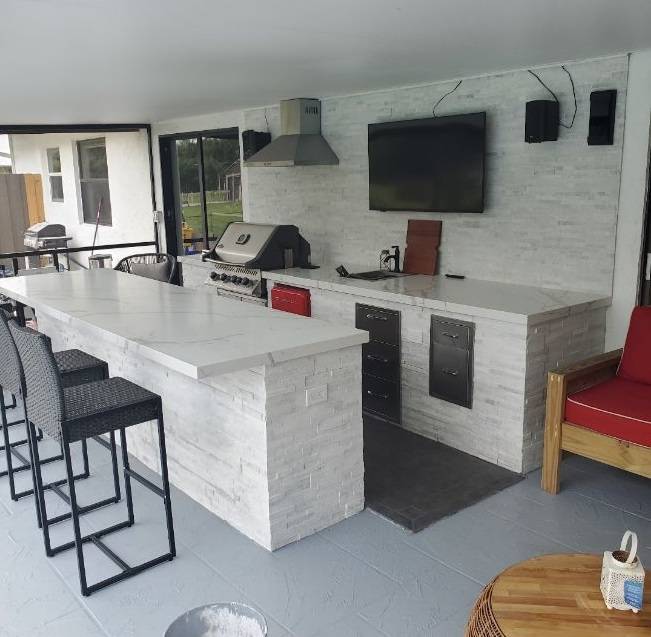 Finished outdoor kitchen with stacked-stone island, built-in grill, and wall-mounted TV