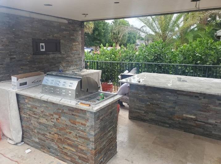 Outdoor kitchen under construction with slate stone veneer counters and a built-in grill
