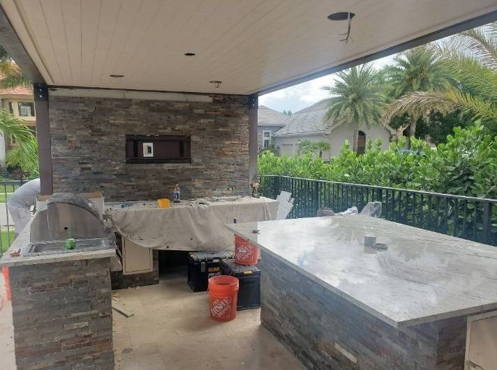 Covered patio outdoor kitchen in progress with stone veneer walls and a concrete countertop island