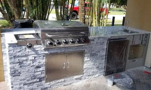 Outdoor kitchen with gray stacked-stone facing, a stainless steel grill, and an under-counter fridge