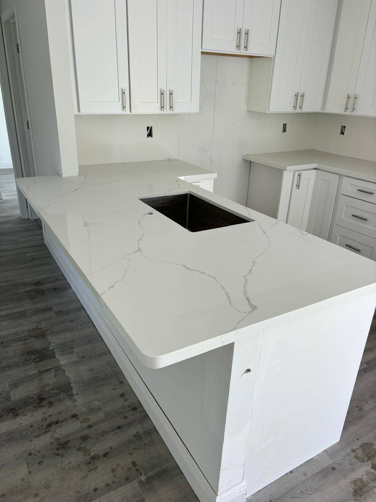 New white quartz kitchen countertop with a veined finish and undermount sink cutout during installation