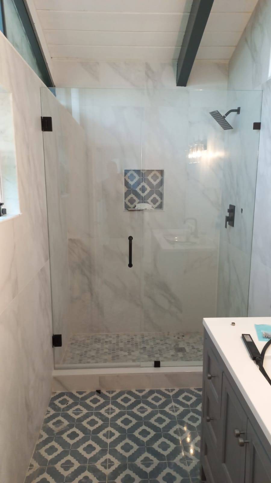 Bathroom remodel with a frameless glass shower, patterned blue floor tile, and a decorative tile niche