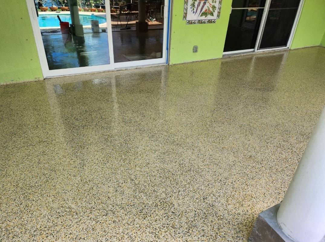 Freshly coated speckled epoxy patio floor beside sliding glass doors and a pool