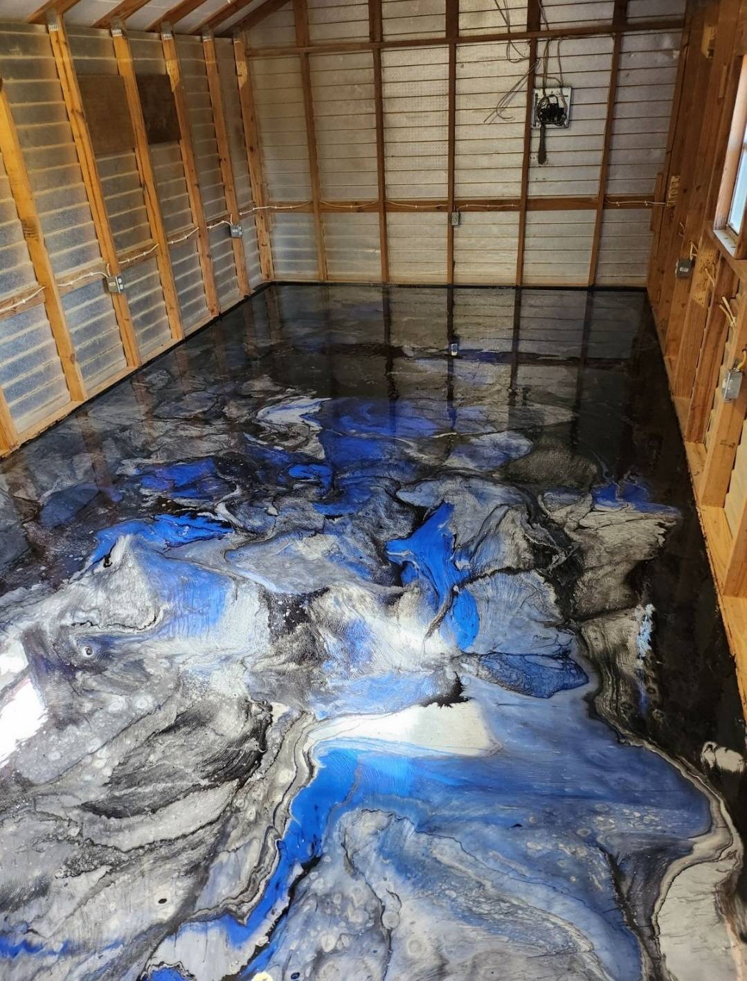 Metallic epoxy floor in blue, black, and silver swirls inside a wood-framed shed